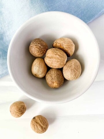 nutmeg in a white bowl on a blue cloth.
