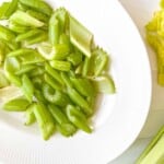 air fried celery pieces on a white plate next to raw celery.