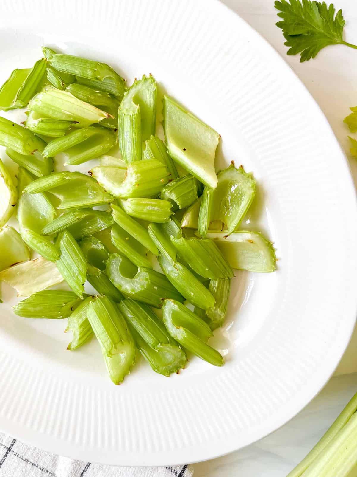 celery pieces on a white plate next to celery leaves.