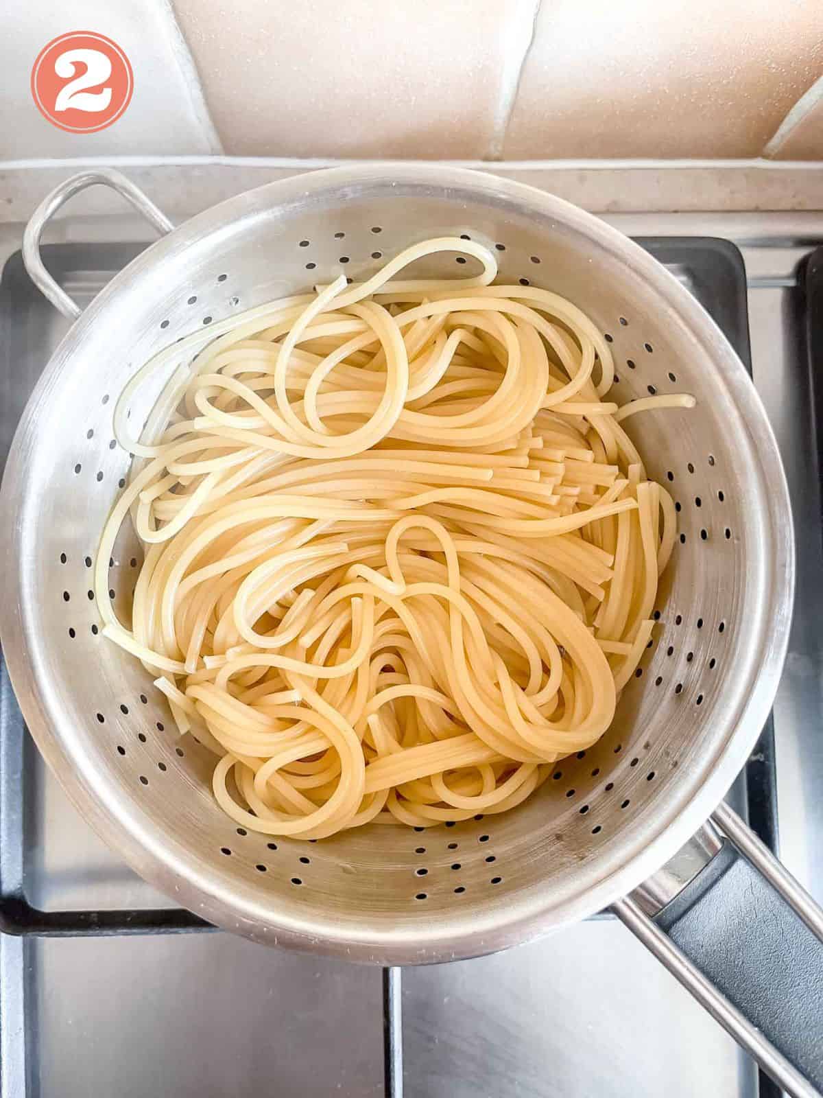 cooked spaghetti pasta in a colander on a stove top labelled number two.