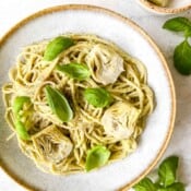 artichoke pesto pasta in a light grey bowl topped with basil leaves and artichoke hearts.