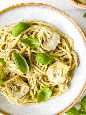 artichoke pesto pasta in a light grey bowl topped with basil leaves and artichoke hearts.