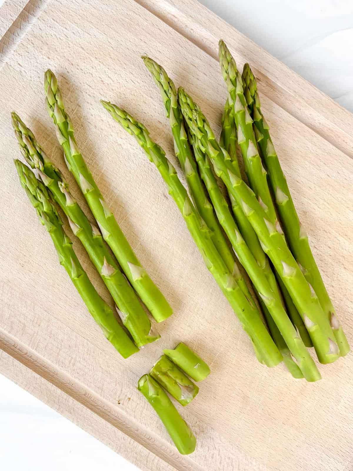 asparagus spears on a wooden board, with half full spears and half snapped spears.
