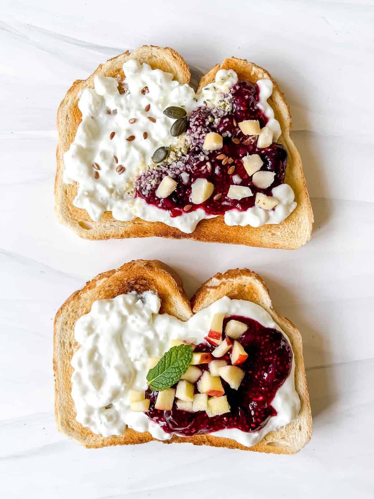 two cottage cheese toasts topped with sweet blueberry jam and nuts, seeds and diced apple.