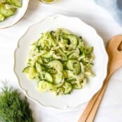 fennel cucumber salad on a white plate next to wooden salad servers and fresh dill.