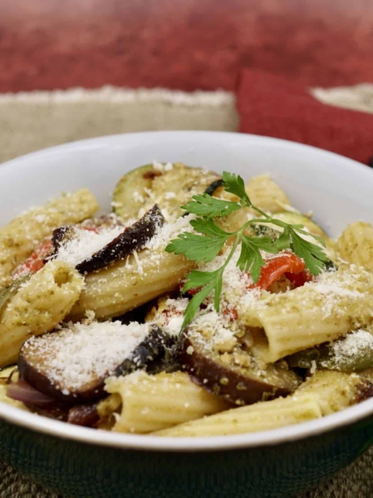 roasted vegetable pesto pasta in a white bowl against a red wall.