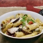 roasted vegetable pesto pasta in a white bowl against a red wall.