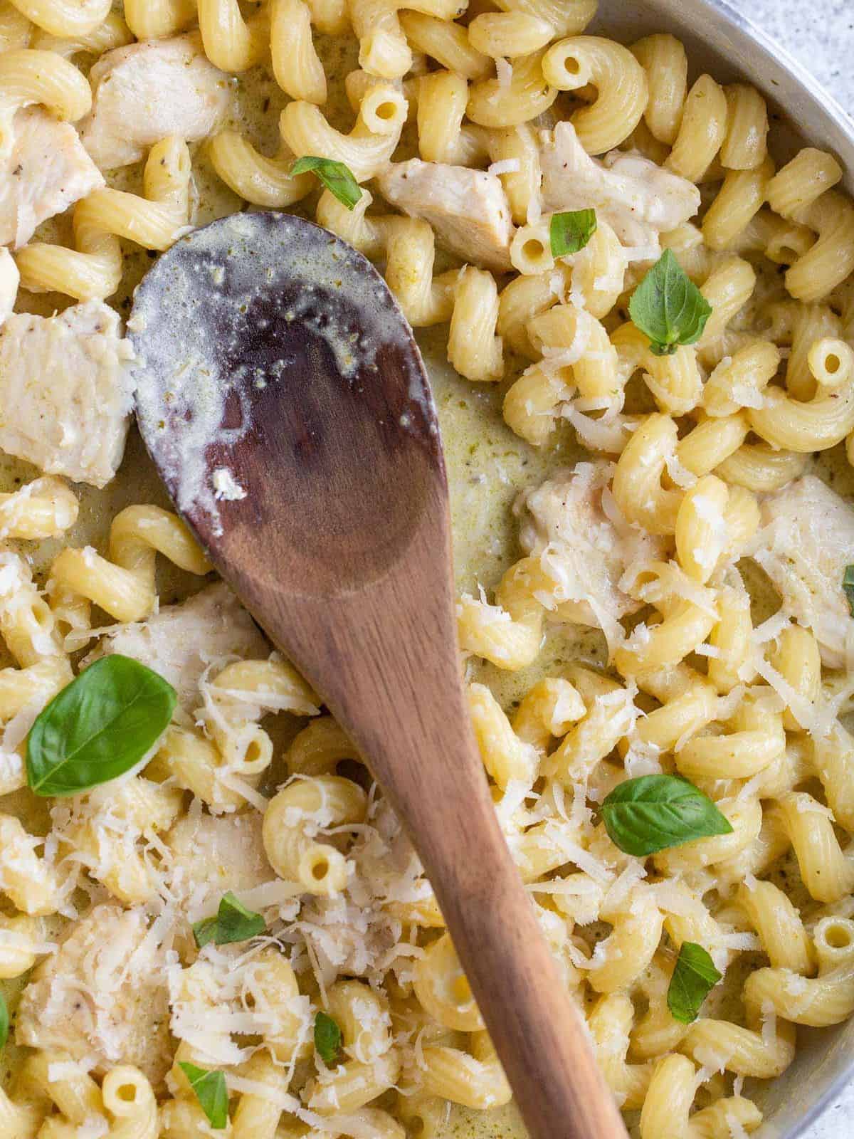 pasta cavatappi in a white skillet with a wooden spoon resting on it.