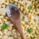 pesto cavatappi with basil leaves and a wooden spoon resting on it.