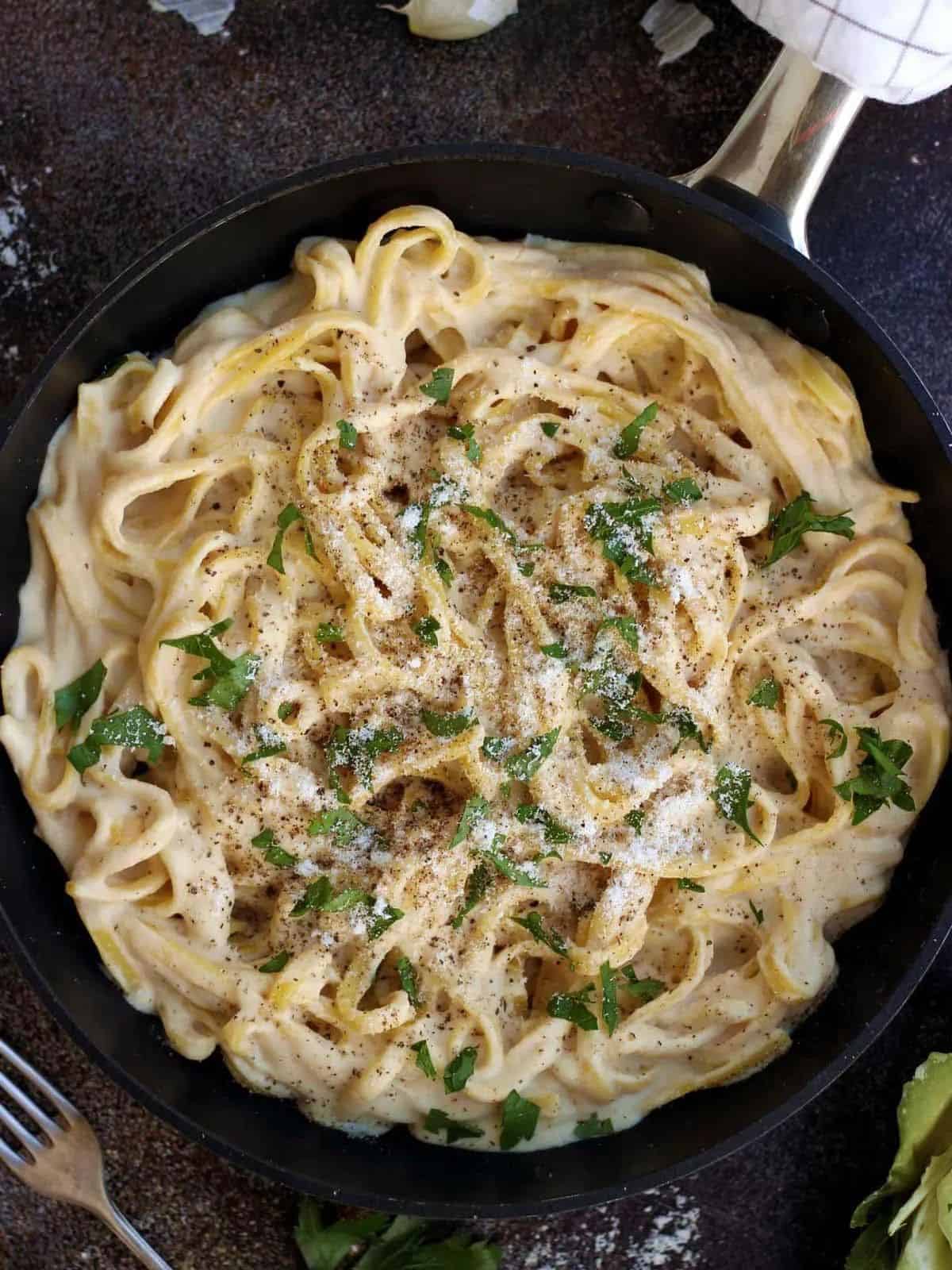 fettuccine alfredo in a black skillet garnished with fresh herbs.