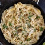 fettuccine alfredo in a black skillet garnished with fresh herbs.