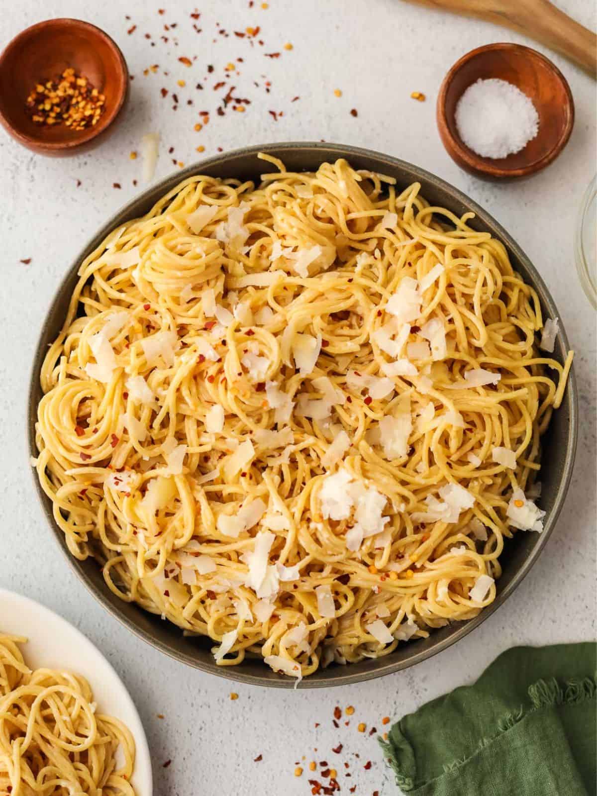 cream cheese pasta in a black bowl next to small bowls of salt and pepper flakes.