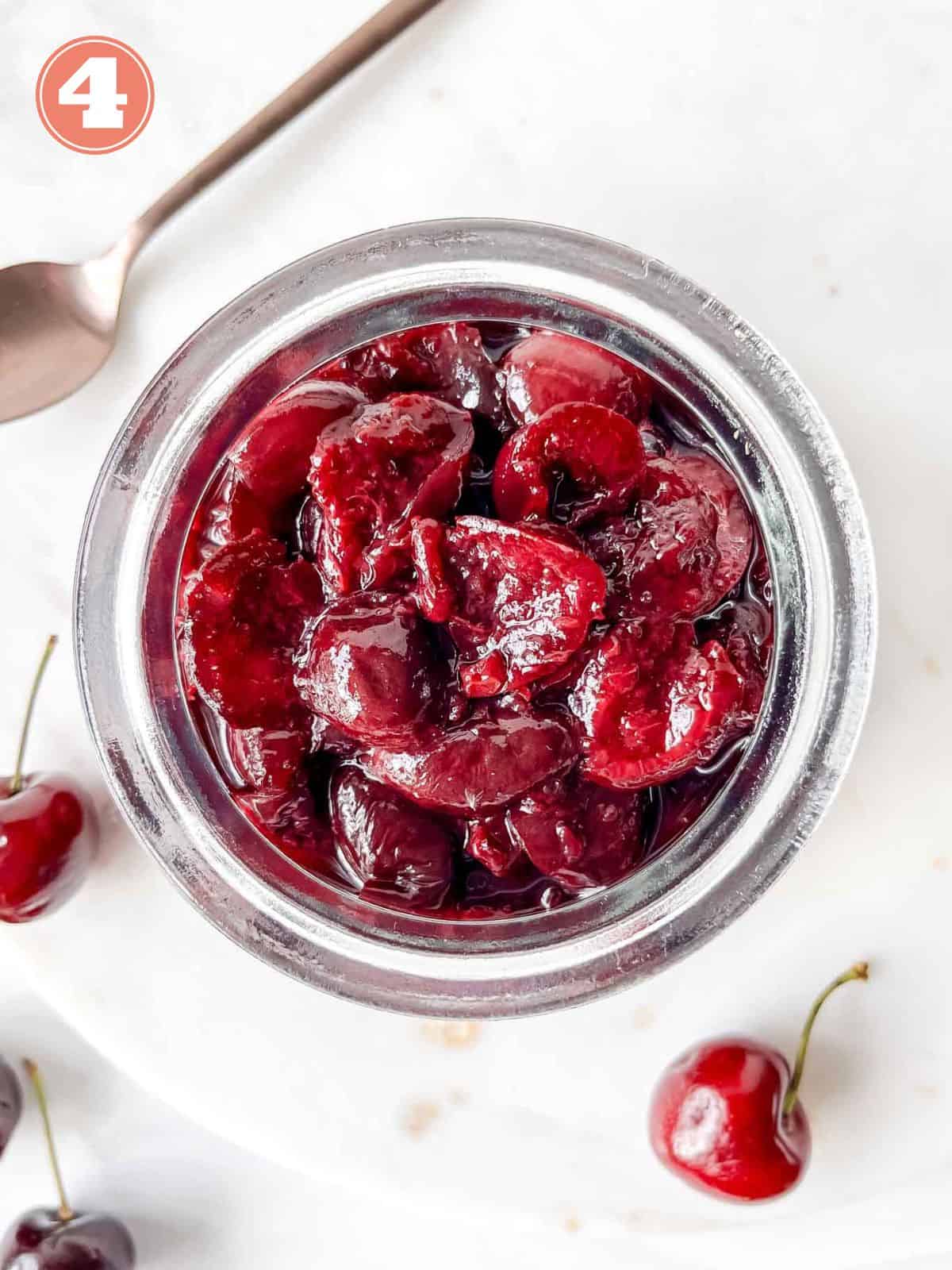 cherry compote in a glass jar next to cherries and a metal spoon labelled number four.