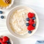 cottage cheese and honey dip in a cream bowl topped with berries next to bowls of honey and berries.