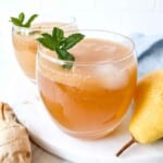 ginger mocktail in two glasses with mint sprigs in them next to root ginger and a pear.