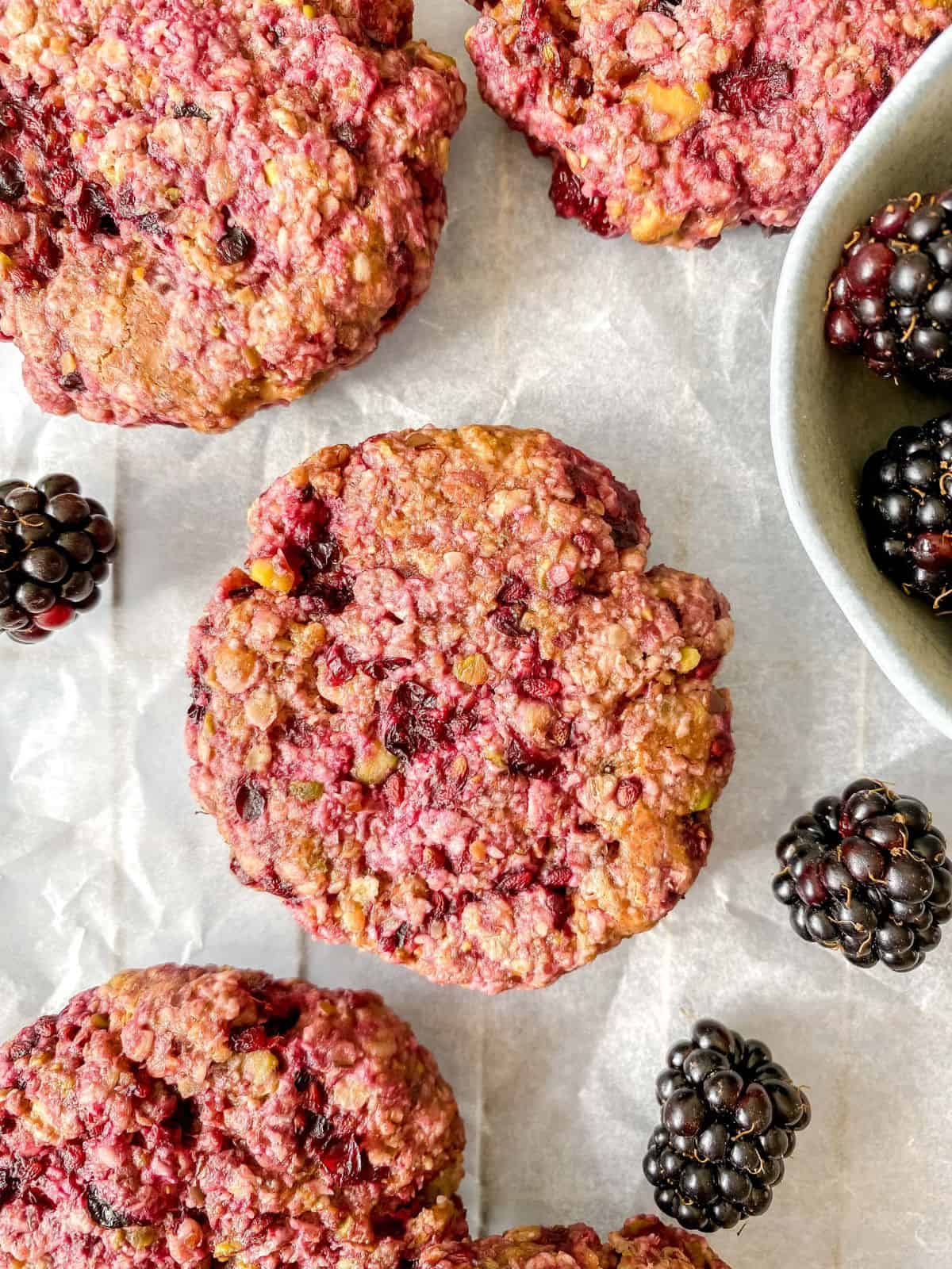 blackberry oatmeal cookies on parchment paper next to fresh blackberries.