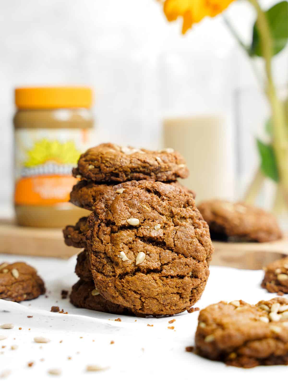 sunflower seed cookies in a stack on a white table with a jar of sunbutter in the background.