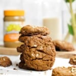 sunflower seed cookies in a stack on a white table with a jar of sunbutter in the background.