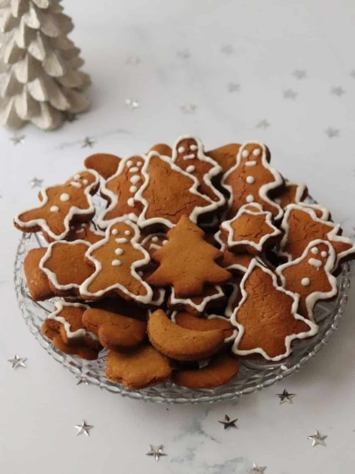 gingerbread cut out cookies in a bowl next to a white Christmas tree.