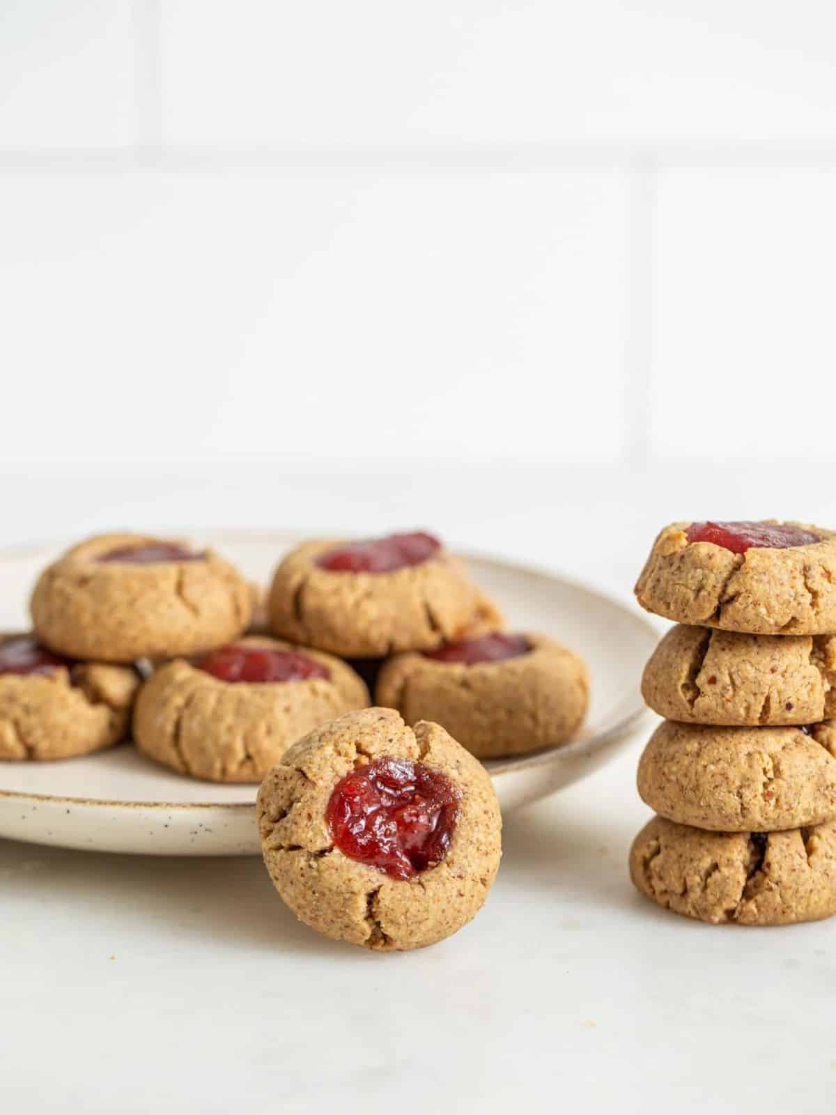 gluten free vegan thumbprint cookies in a stack and on a cream bowl.