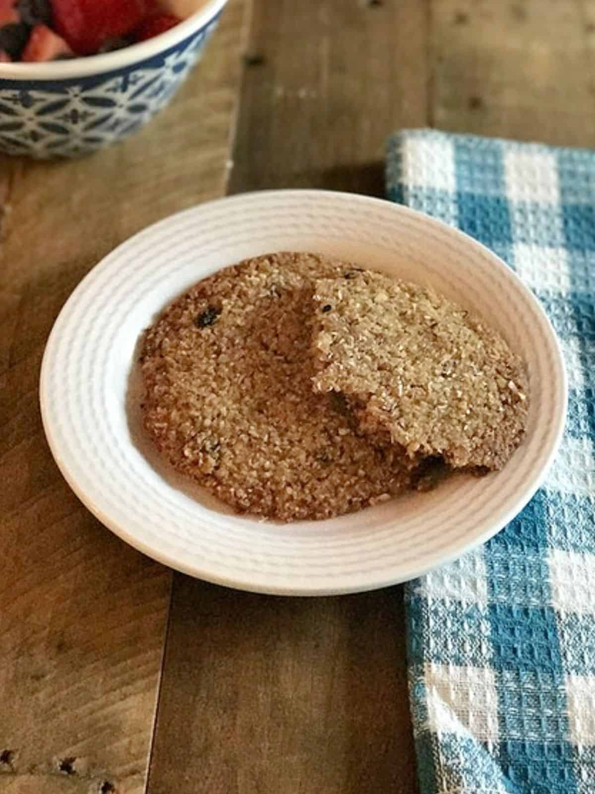 large breakfast cookies on a white plate next to a blue checked cloth on a wooden table.