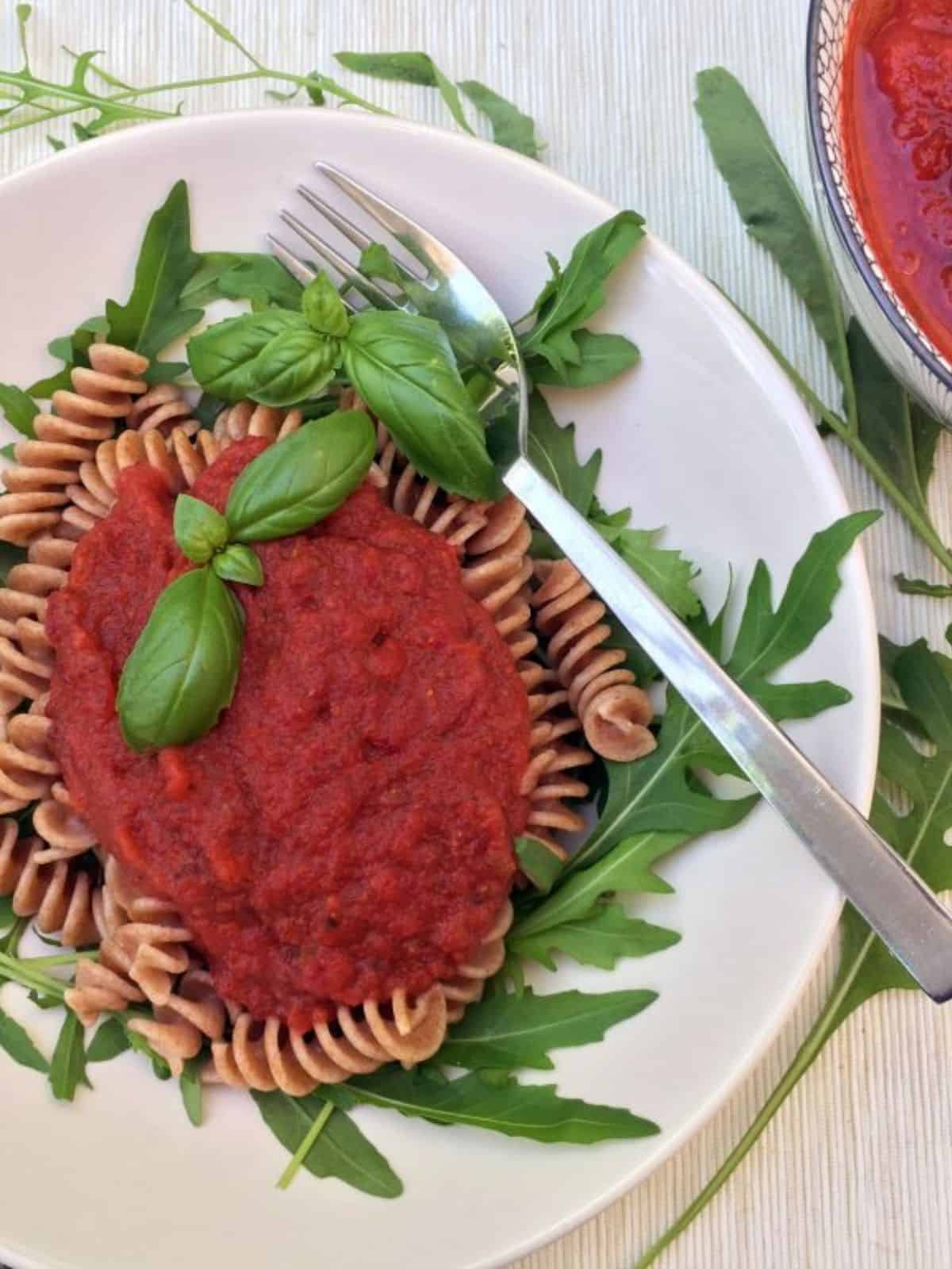 nomato sauce on top of pasta on a white plate with basil leaves and a fork.