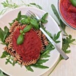 nomato sauce on pasta on a white plate with a fork and basil leaves.