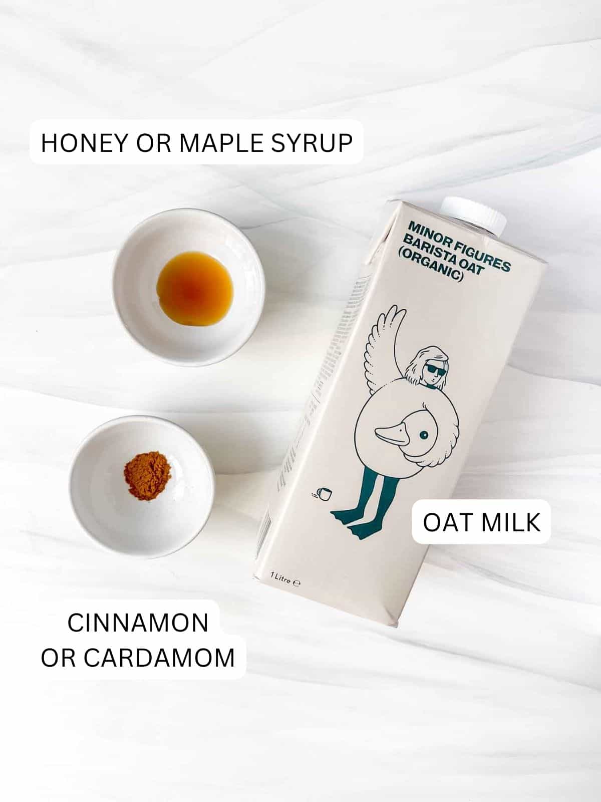 labelled oat milk in a carton, honey or maple syrup and cinnamon or cardamom in small bowls.
