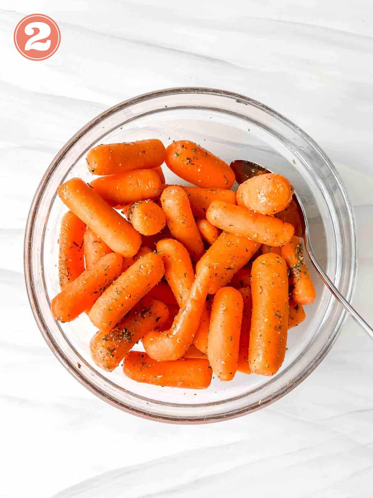 baby carrots mixed with herbs in a glass bowl with a spoon labelled number two.