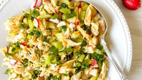 chicken salad without mayo on a white plate with a spoon next to parsley and radishes.