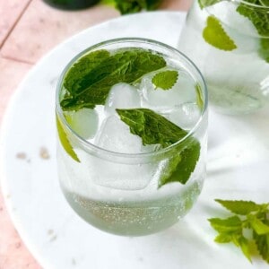 hugo spritz mocktail in two glasses on a marble board on a pink table.