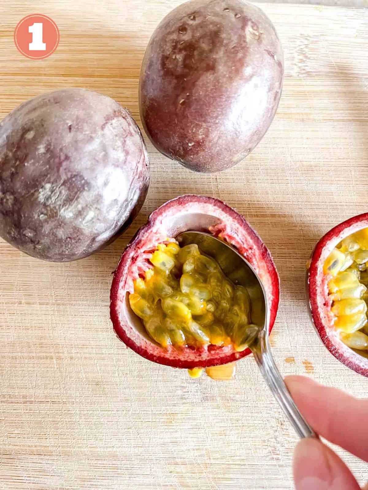 passion fruit on a wooden chopping board with passion fruit pulp being scooped out of one with a spoon labelled number one.
