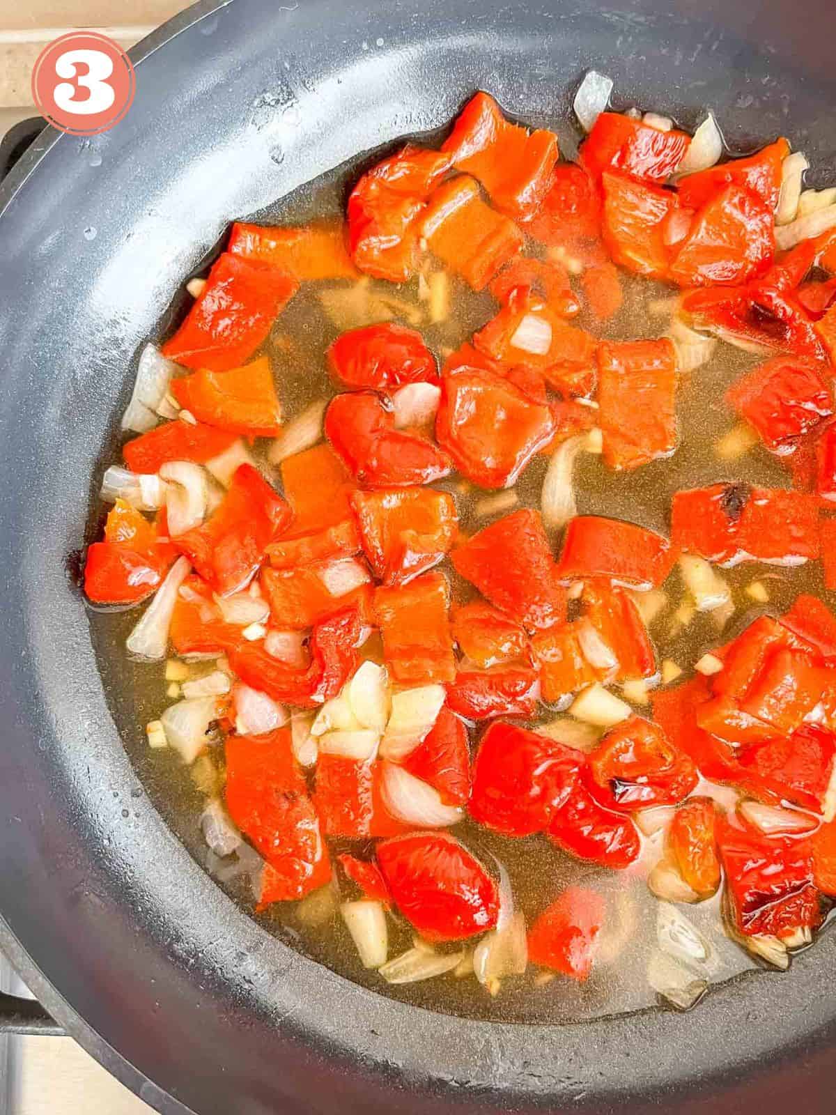 diced red bell peppers, onion and garlic in vegetable stock in a black skillet labelled number three.