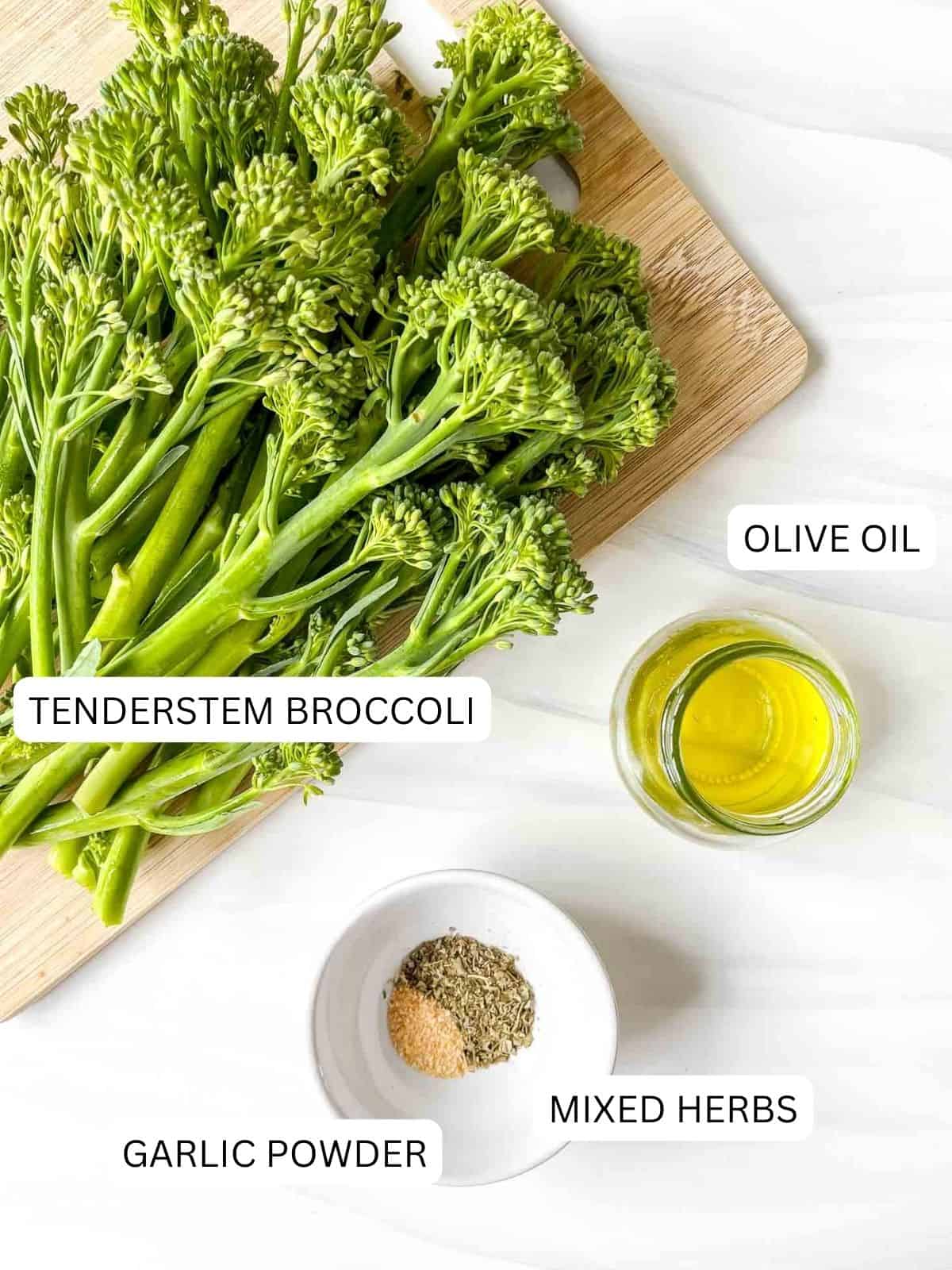 individually labelled tenderstem broccoli on a wooden board, mixed herbs and garlic powder in a white bowl and olive oil in a glass jar.