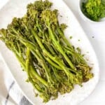 roasted tenderstem broccoli on a light grey plate next to a small bowl of herbs.