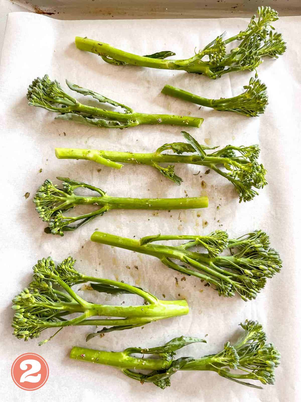 tenderstem broccoli drizzled with olive oil and sprinkled with herbs on a lined baking sheet labelled number two.
