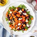 roasted sweet potato beetroot salad on a white plate with a fork on a blue cloth next to beets.