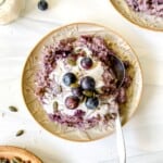 blueberry quinoa breakfast bake with a spoon in it on a light brown plate next to a bowl of pumpkin seeds.