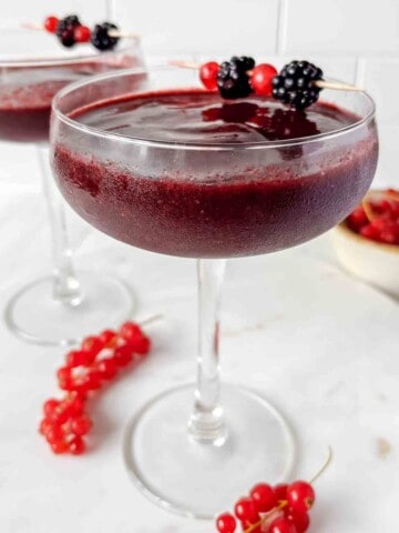 frozen berry mocktail in two glasses with a bowl of red currants in the background.