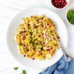 roasted cauliflower quinoa salad on a white plate with a spoon next to a blue cloth and bowls of herbs and pomegranates.