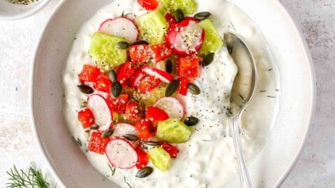 savory cottage cheese bowl with a spoon in it next to a bowl of hemp seeds, dill and blue cloth.