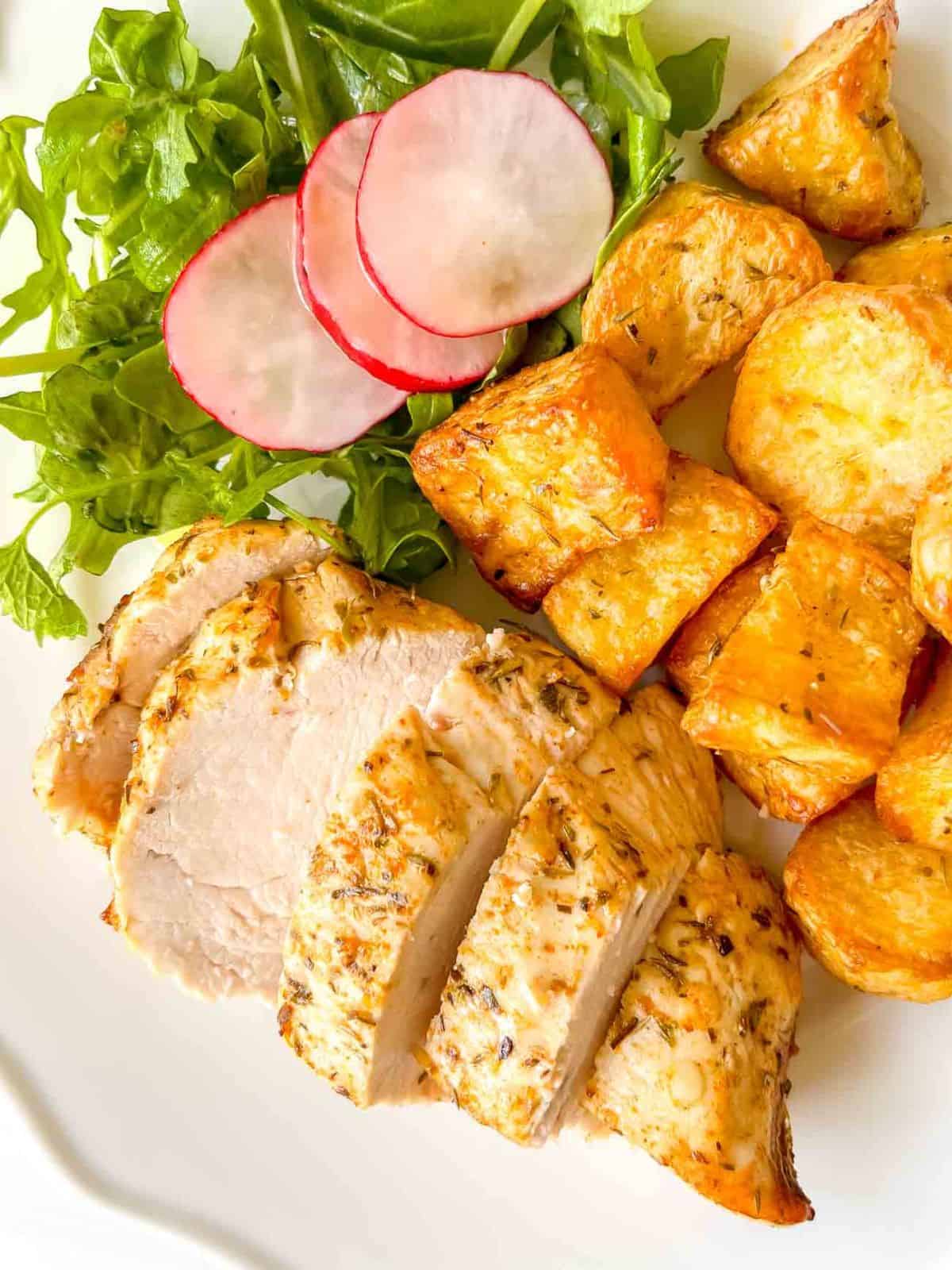 air fryer chicken breast and potatoes with arugula and radishes on a white plate.