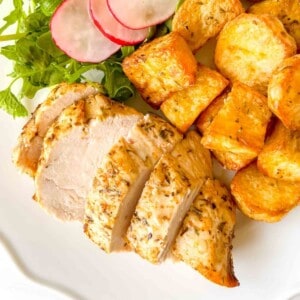 air fryer chicken breast and potatoes with arugula and radish on a white plate.