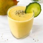 mango cucumber smoothie in a glass next to a mango.