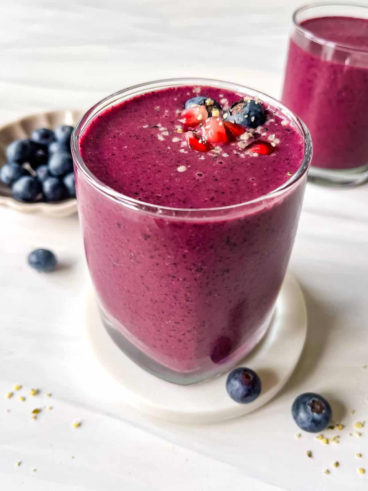 blueberry smoothie in two glasses next to a small bowl of blueberries.