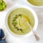 celery zucchini soup in two white bowls next to a small bowl of celery and blue cloth.