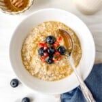 honey porridge in a white bowl topped with fruit next to a small bowl of honey.