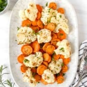 roasted carrots and cauliflower on a light grey plate next to a bowl of herbs.