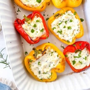 ricotta stuffed peppers in a white baking dish garnished with herbs.