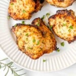 air fryer rosemary chicken thighs on a white plate next to a rosemary sprig.